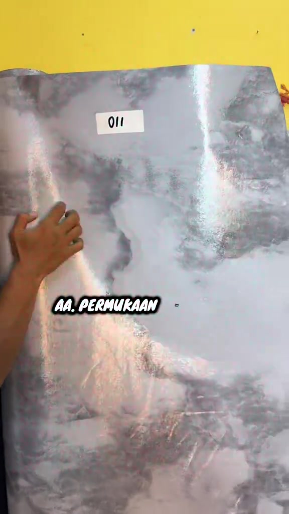 Tangan menyentuh permukaan tikar getah PVC corak marmar kelabu yang berkilat untuk menunjukkan teksturnya