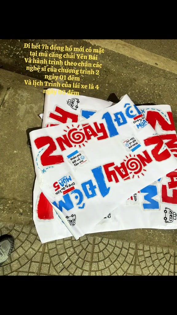 Những lá cờ vải in logo 2 Ngày 1 Đêm mùa 5 màu đỏ và xanh đặt chồng trên nền gạch, đạo cụ của đoàn ghi hình