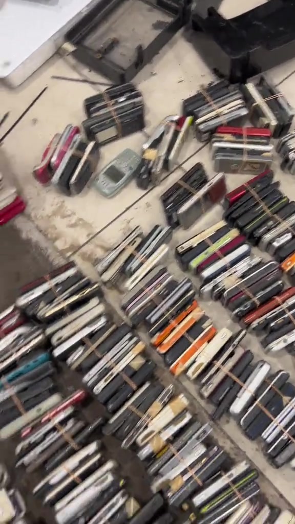 Gulungan phone lama diikat getah disusun berlapis di lantai, unit-unit yang hanya layak nilai pukal
