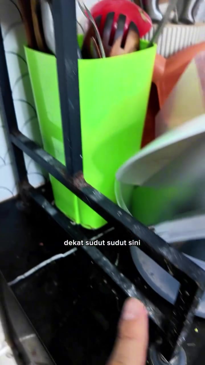 Bintik karat pada sudut rangka rak pinggan besi bersalut hitam berhampiran bekas sudu