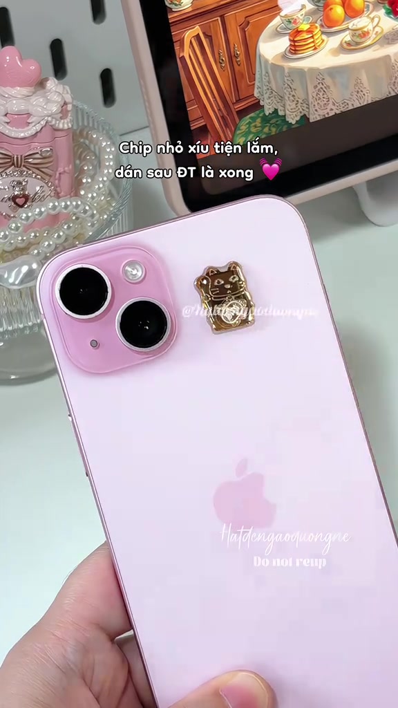 Miếng chip mạ vàng hình mèo dán cạnh cụm camera trên mặt lưng màu hồng của một chiếc iPhone