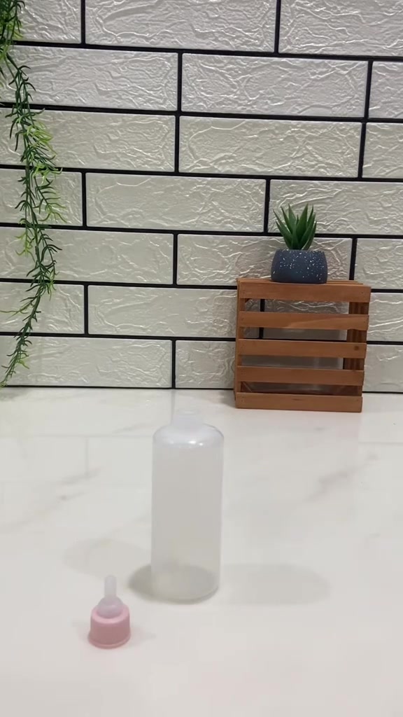 Botol susu kucing lut putih dengan puting merah jambu diletakkan di atas meja putih