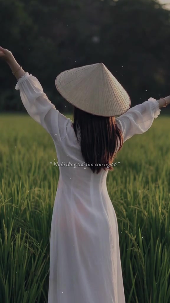 Clip fan nhạc Gạo Của Ta: cô gái mặc áo dài trắng, đội nón lá, đứng giữa ruộng lúa nhìn từ phía sau, hai tay dang cao