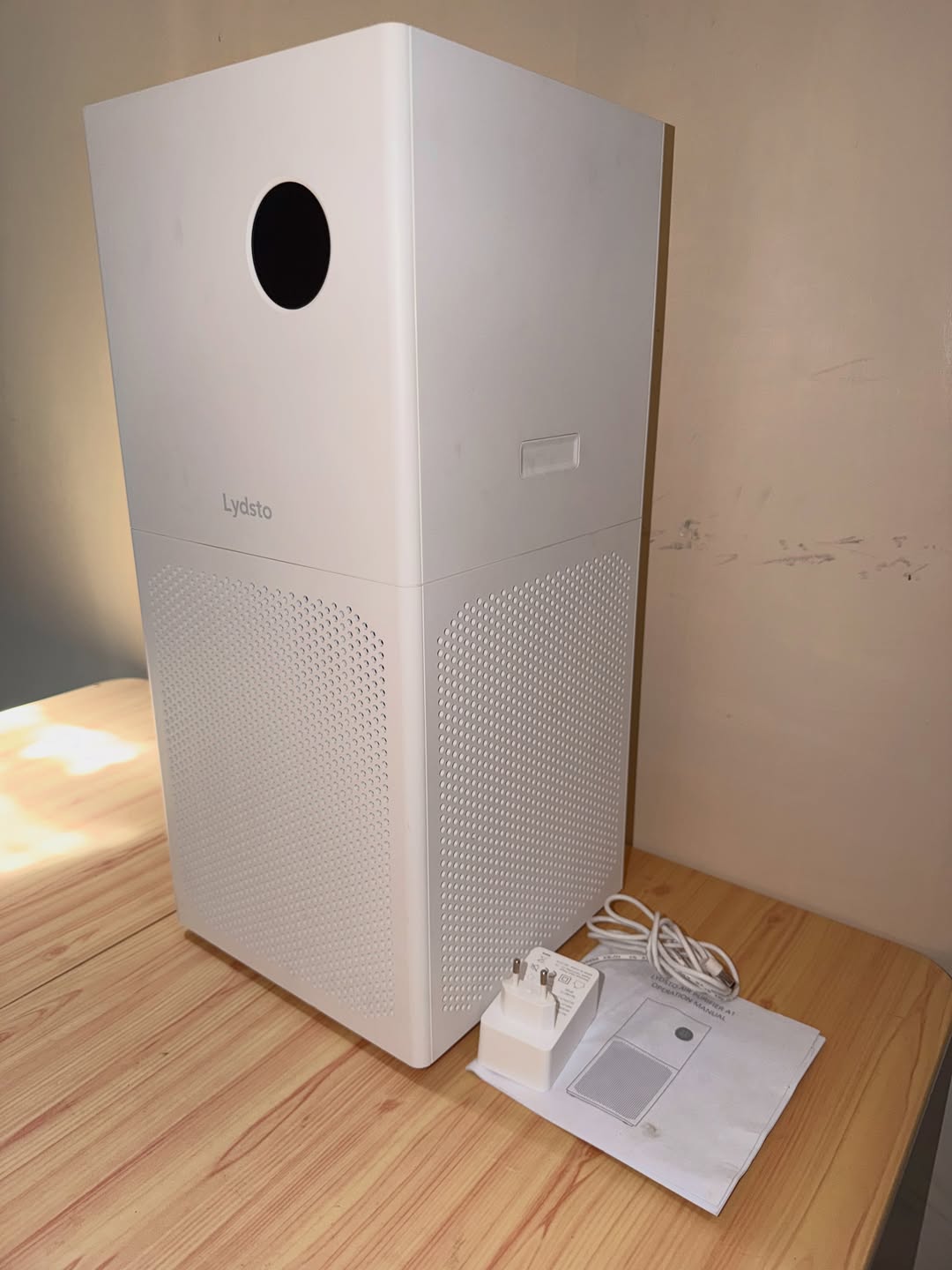 Air purifier putih dengan palam kuasa dan buku manual pengguna di sebelahnya atas meja kayu