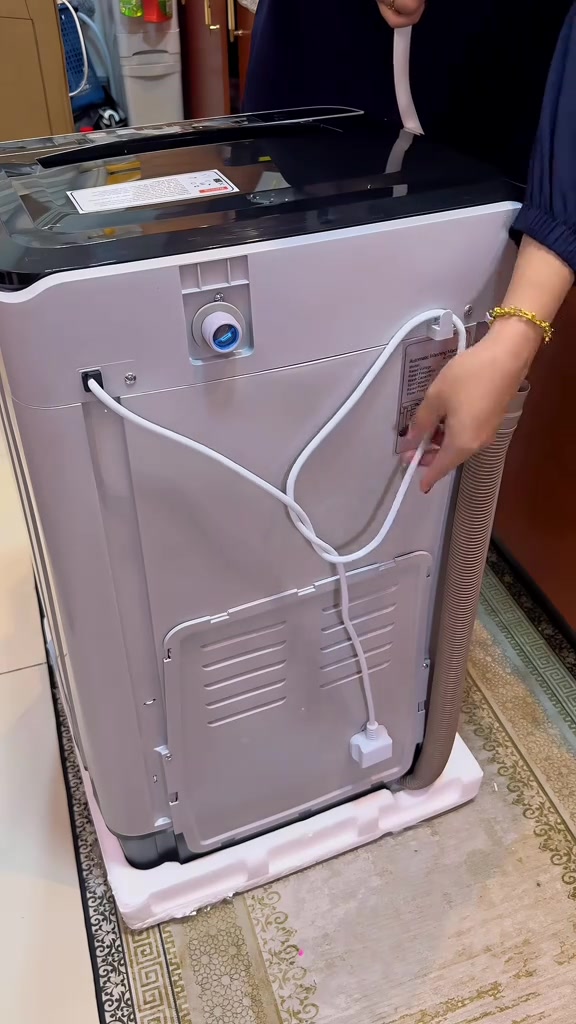 Bahagian belakang mesin basuh compact menunjukkan hos buang air, injap masuk air dan plug tergantung