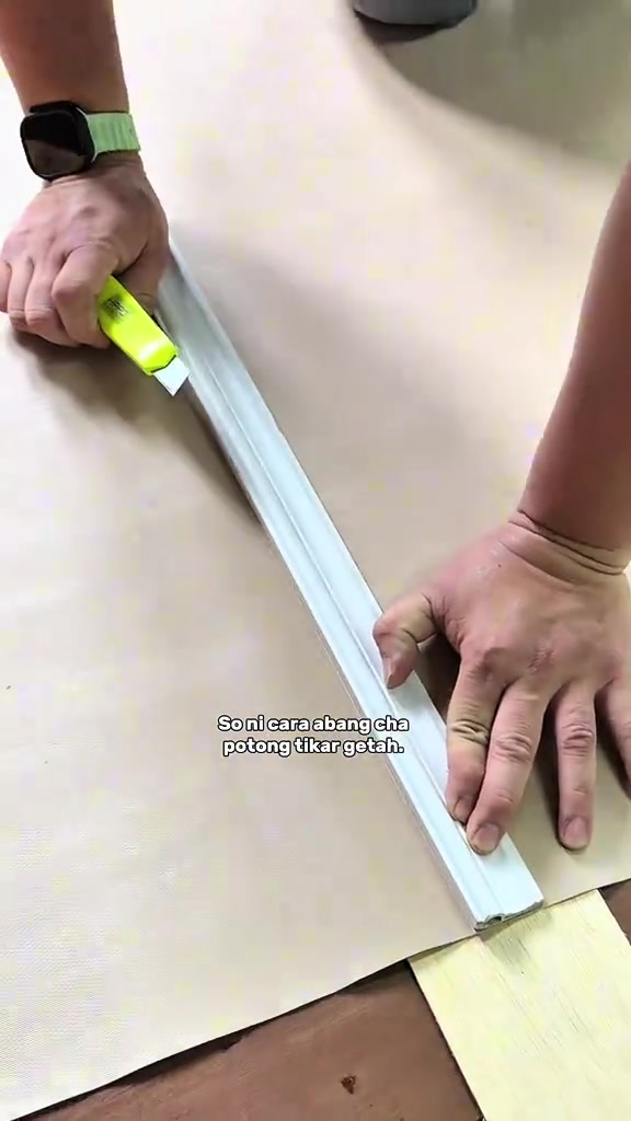 Dua tangan memotong tikar getah menggunakan pembaris aluminium dan pisau cutter