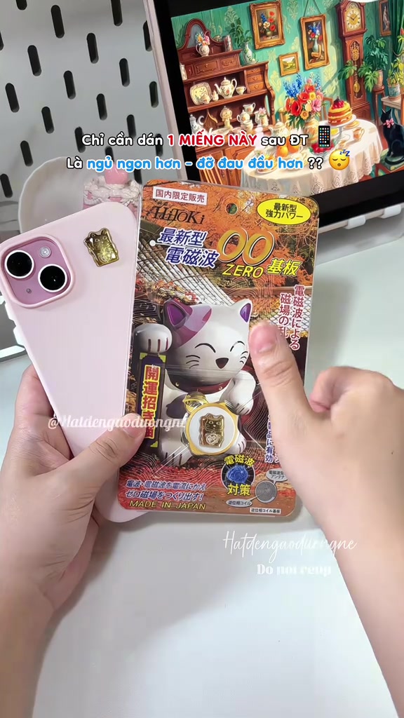 Vỉ giấy in chữ Nhật của miếng dán HITOKI hình mèo mèo may mắn, đặt cạnh chiếc ốp lưng màu hồng có dán chip mạ vàng