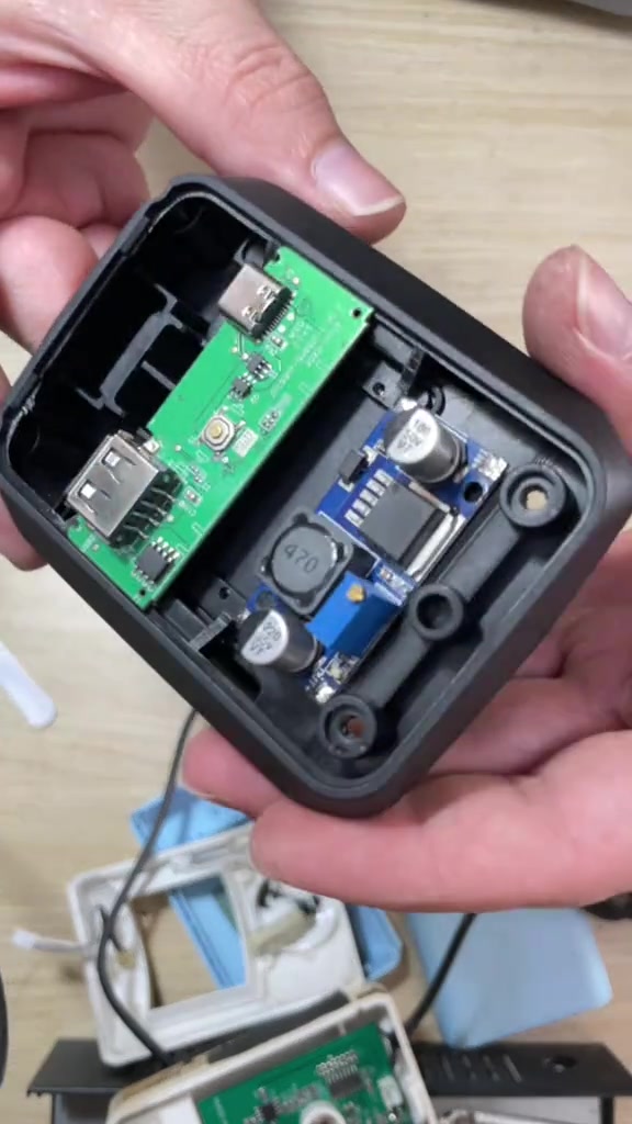 Vỏ đế chuyển nguồn mở ra, lộ bảng mạch cổng USB màu xanh lá và module chuyển đổi màu xanh dương với tụ điện và cuộn cảm