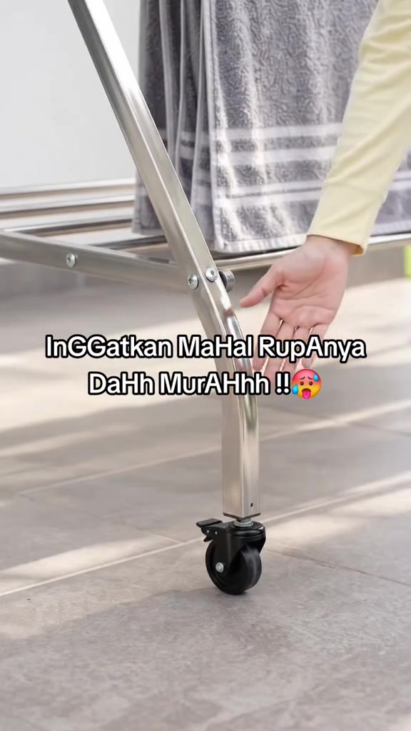 Kaki rak jemuran stainless steel beroda dengan tuala kelabu disidai di bar atas