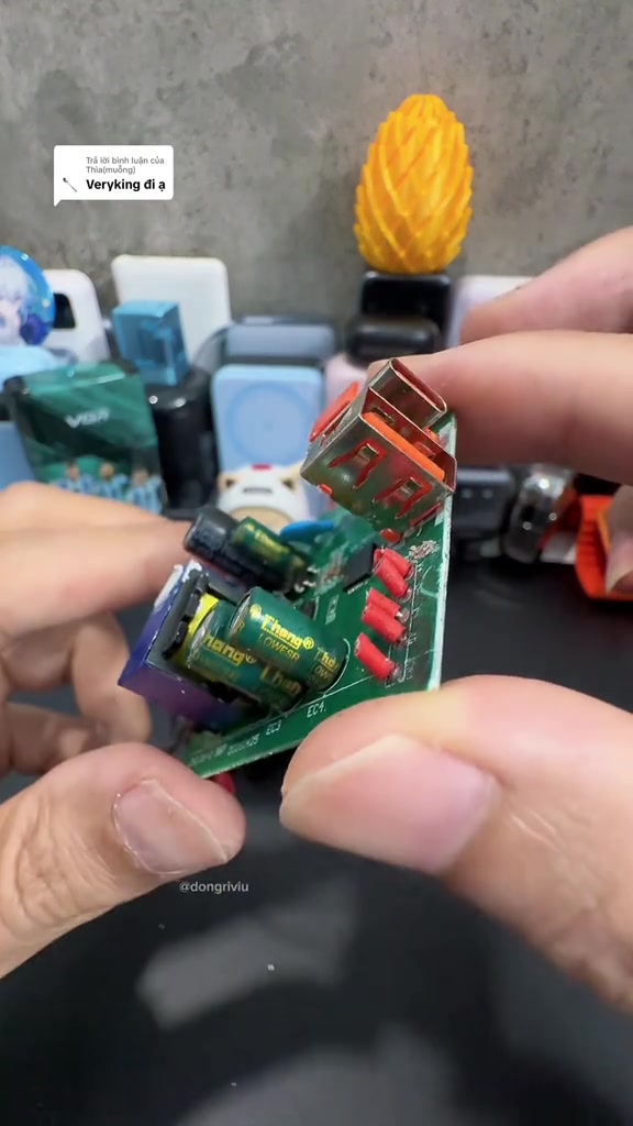 Bo mạch của một củ sạc nhanh tháo vỏ cầm trên tay, nhìn rõ tụ điện và cụm cổng USB