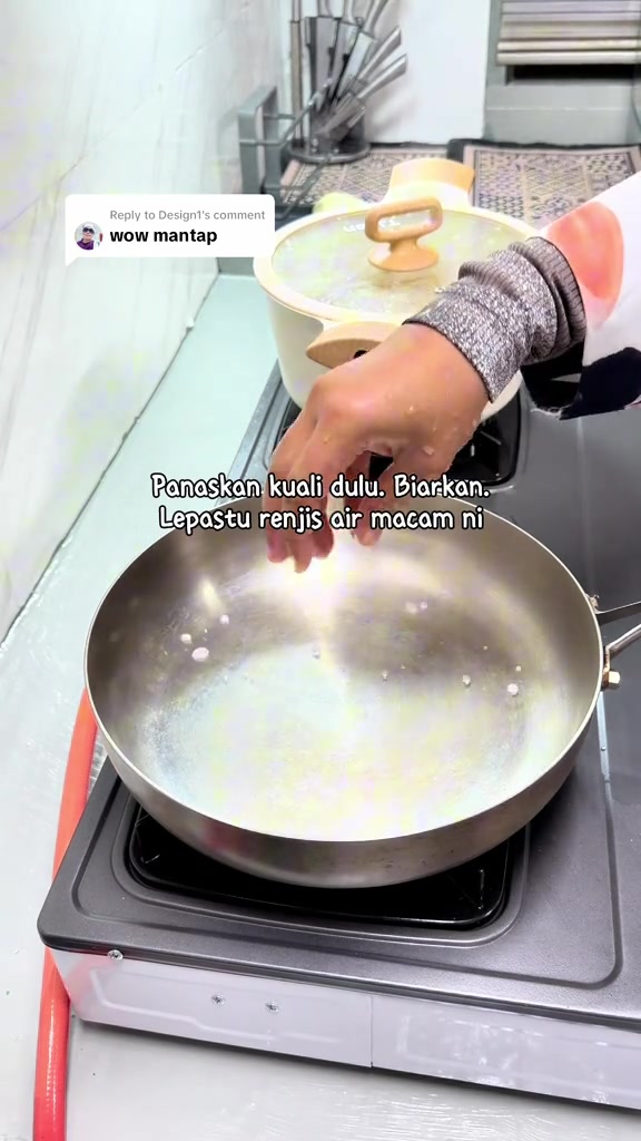 Tangan merenjis beberapa titik air ke dalam kuali stainless steel yang dipanaskan di atas dapur gas