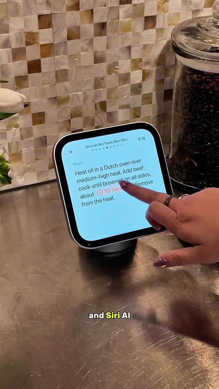 Bàn tay chạm vào màn hình Apple HomeView đang mở bước 5 của một công thức nấu ăn, đặt trên mặt bếp kim loại