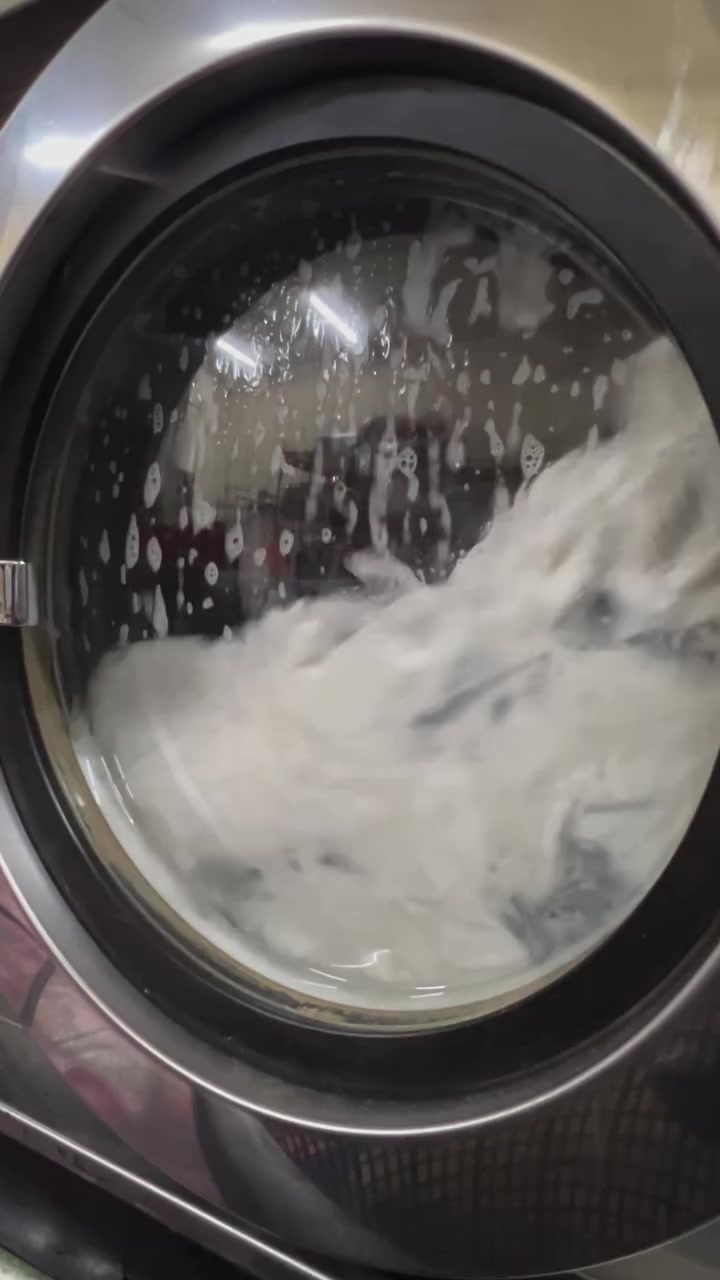 Drum mesin basuh front load berisi buih sabun dan cucian sedang berpusing