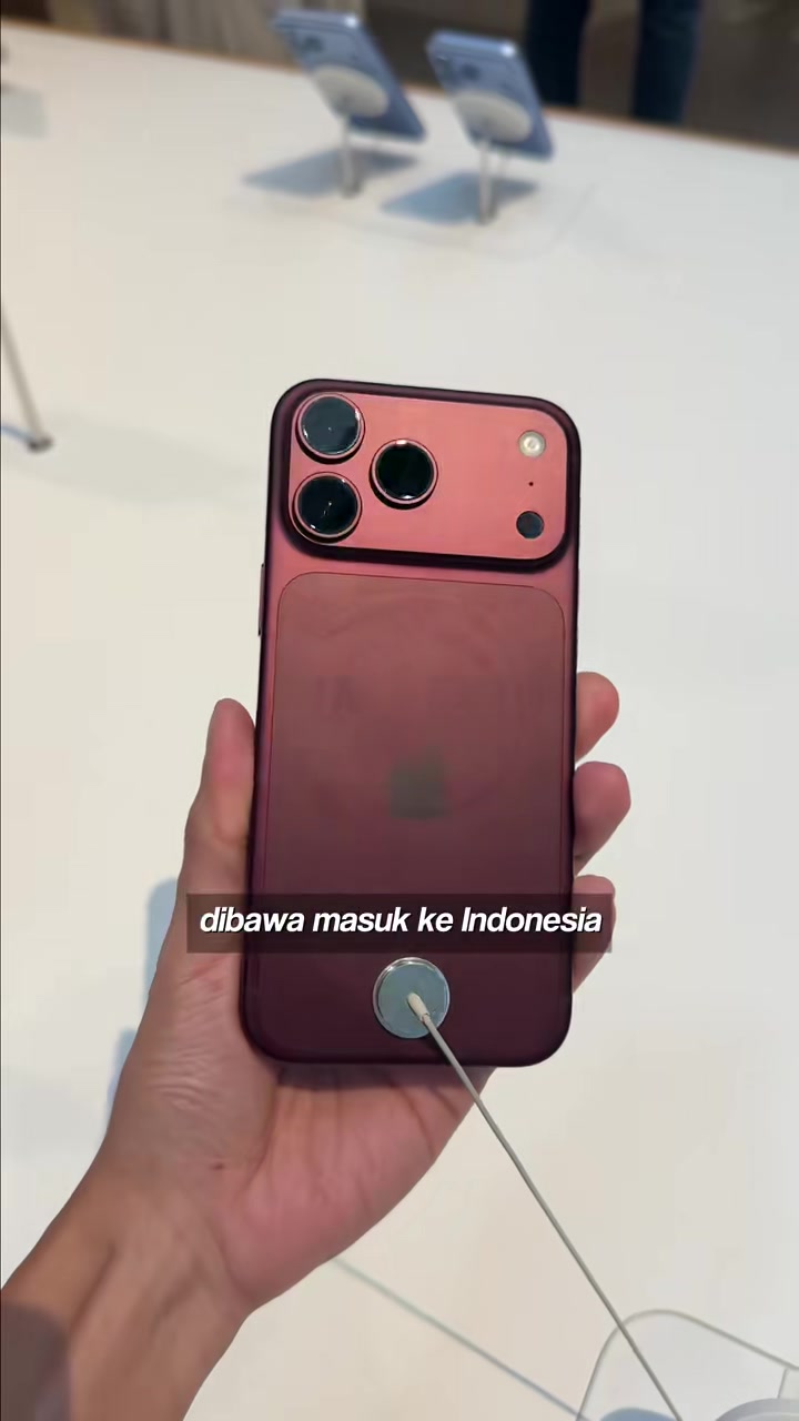 Tangan memegang iPhone 18 Pro warna merah marun dengan tiga kamera di dalam kedai Apple