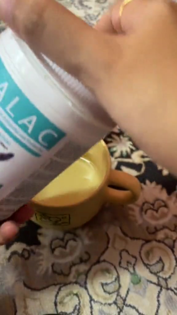 Tangan menuang serbuk susu kucing dari bekas berlabel Midalac ke dalam cawan kuning kecil