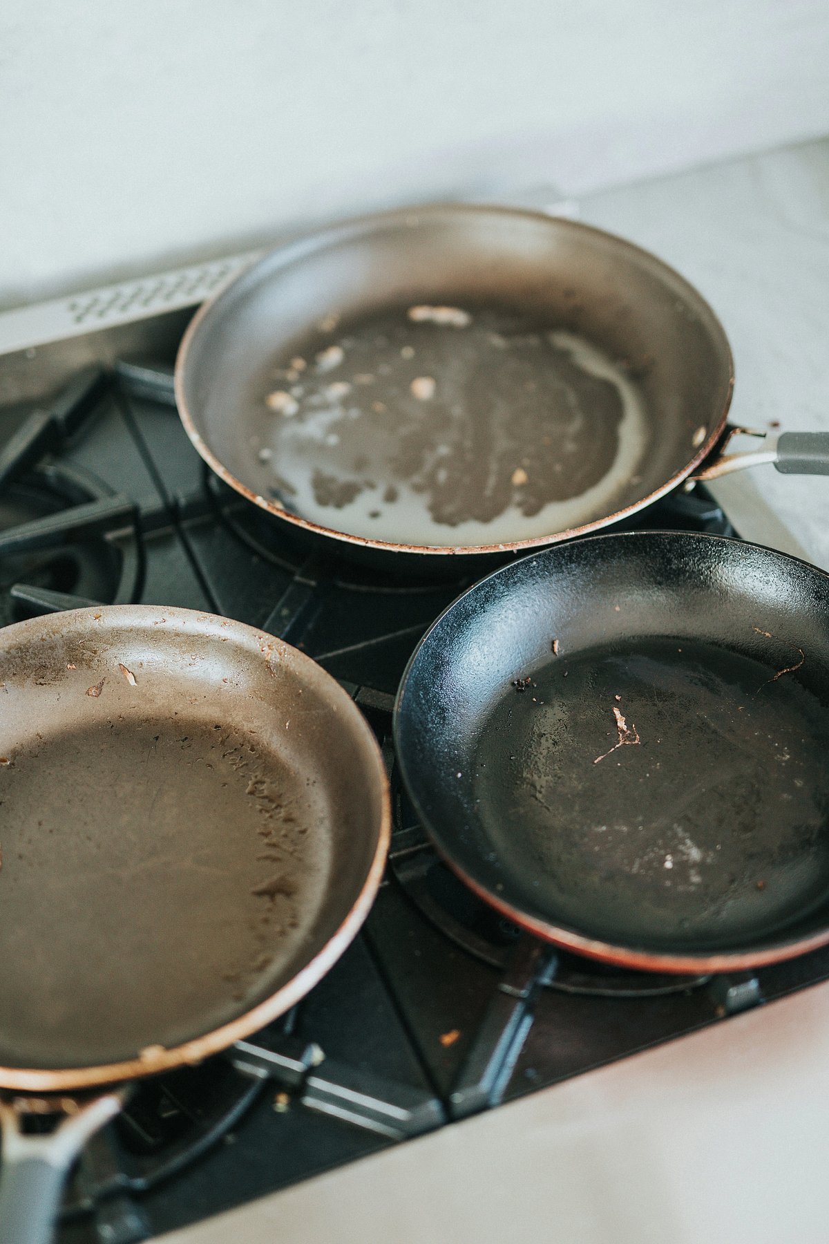 Tiga kuali non-stick terpakai dengan coating lusuh dan berubah warna di atas dapur gas