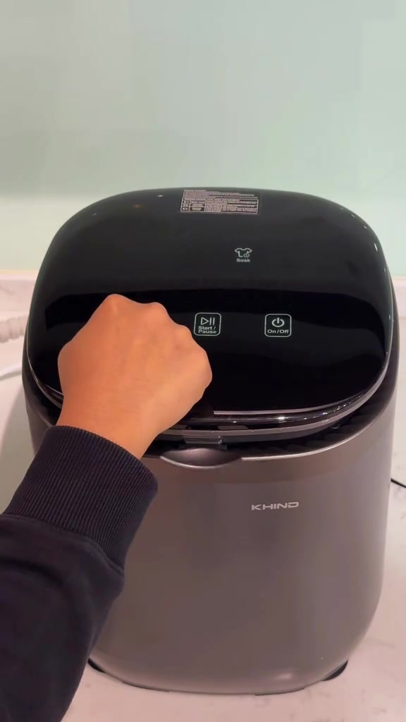 Tangan menekan butang panel digital mesin basuh mini Khind berwarna kelabu gelap
