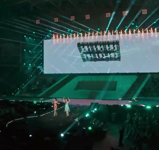 Sân khấu ánh xanh của tiết mục song ca nhìn từ khán đài trên, hai bóng ca sĩ đứng giữa nhà thi đấu dưới màn LED treo cao