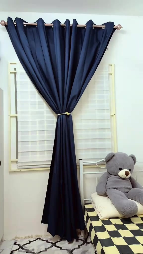 Langsir navy digantung bertindih di atas bidai putih pada tingkap bilik tidur, dengan patung bear di atas katil