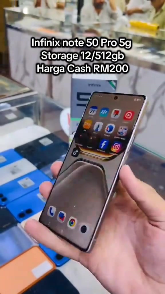 Telefon Infinix Note 50 dipegang tangan di dalam kedai dengan deretan telefon pelbagai warna di latar belakang