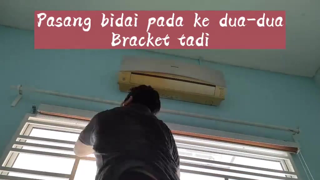 Pandangan belakang seseorang memasang bidai pada bracket di atas tingkap bawah unit aircond