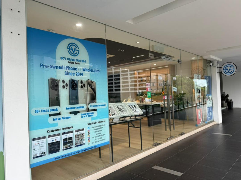 Hadapan kedai SCV Global dengan banner biru bertulis Pre-owned iPhone Wholesales Since 2014 dan deretan meja pameran di dalam