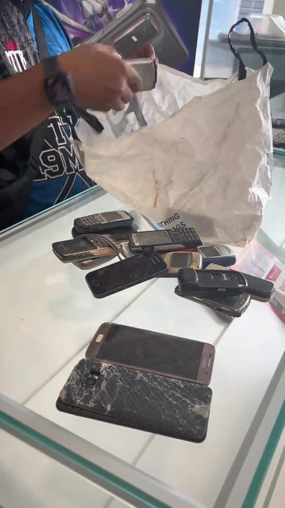 Longgokan phone lama pelbagai model diletakkan atas kaunter kaca kedai untuk dinilai trade-in