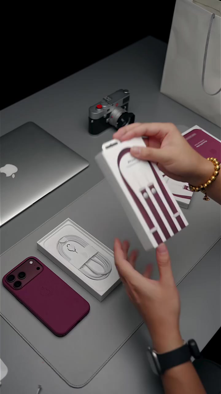 Bàn mở hộp iPhone 18 Pro Max với máy màu burgundy, khay cáp USB-C và hộp ốp lưng đặt trên bàn xám