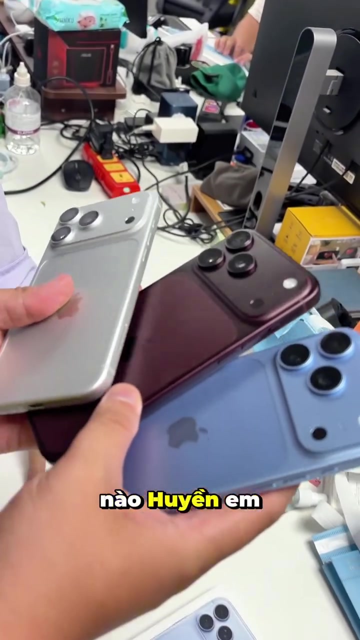 Ba chiếc iPhone 18 Pro Max màu bạc, đỏ burgundy và xanh đặt chồng lên nhau trong lòng bàn tay tại quầy
