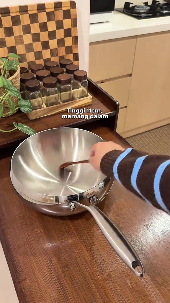 Kuali wok stainless steel berpermukaan berkilat dengan pemegang besi di atas counter kayu