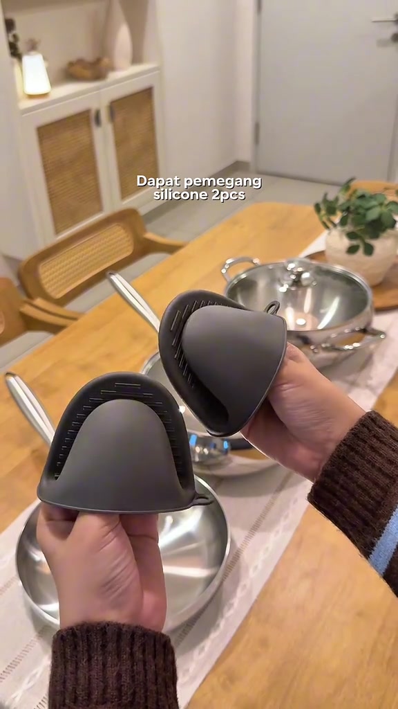 Dua pemegang silicone kelabu untuk pemegang kuali stainless steel dipegang dengan tangan