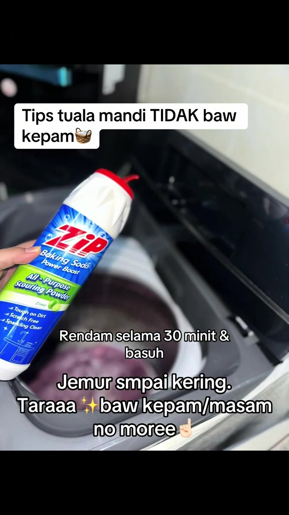 Tangan memegang botol Zip Baking Soda di atas mesin basuh top load