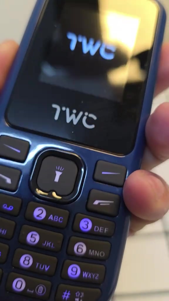 Telefon butang TWC warna biru di tangan dengan kekunci nombor besar dan butang lampu suluh di tengah