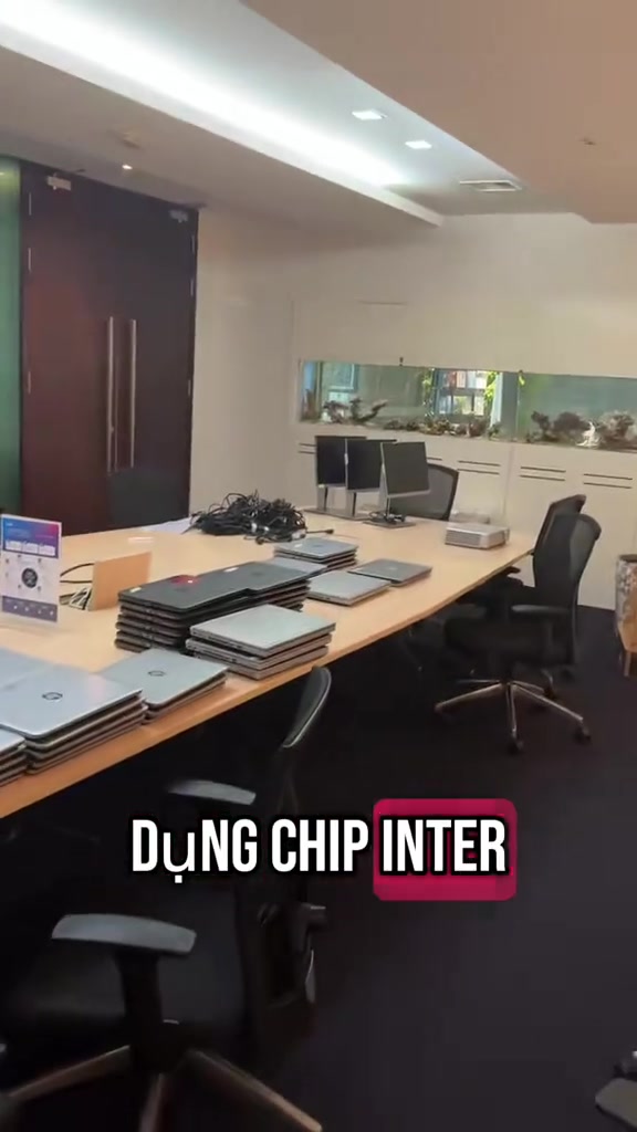 Hàng chục laptop cũ xếp thành chồng trên bàn dài trong một văn phòng thanh lý
