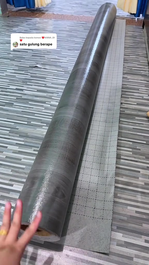 Segulung tikar getah corak kayu kelabu dibaringkan di lantai, bersebelahan hamparan bahagian belakangnya yang bercorak grid
