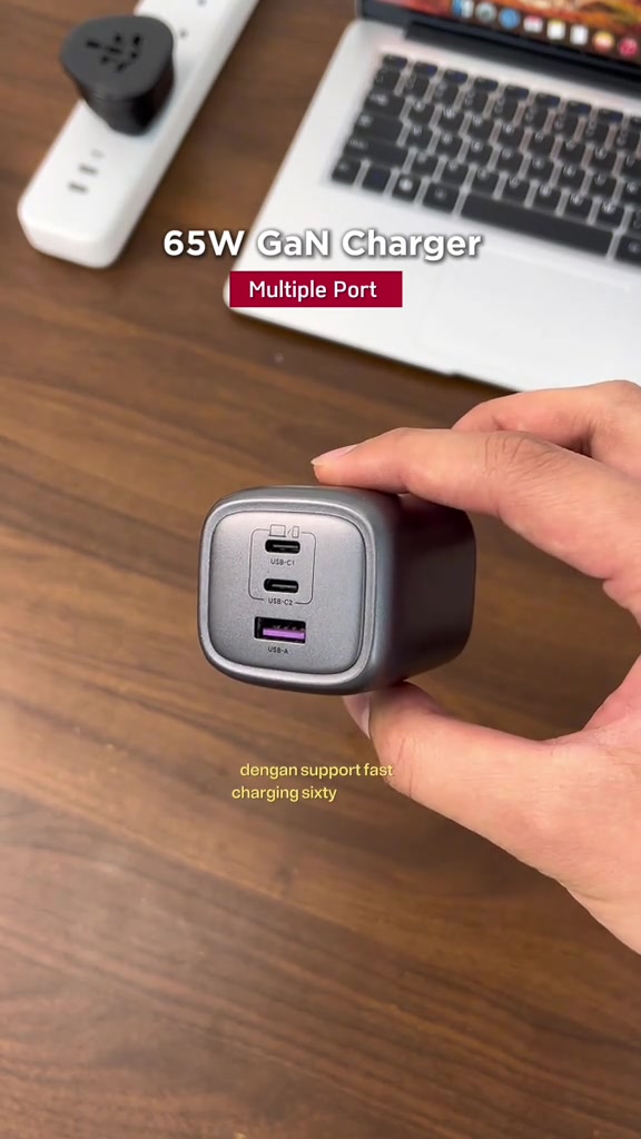 Pengecas UGREEN 65W GaN warna kelabu dengan dua port USB-C dan satu port USB-A dipegang di tangan
