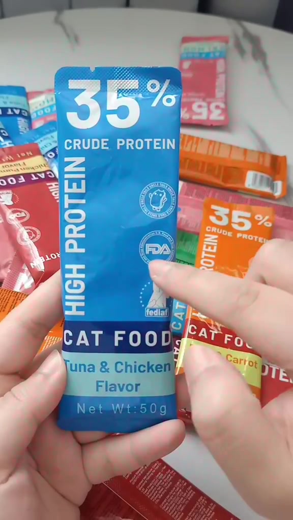 Sachet snack kucing biru berlabel 35% crude protein perisa tuna & chicken 50g dipegang dua jari