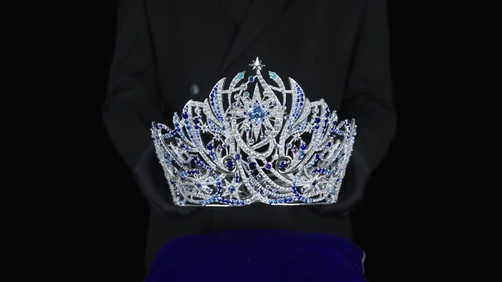 Người mặc trang phục đen nâng vương miện Miss Universe Vietnam 2026 trên đệm xanh, khuôn mặt nằm ngoài khung hình