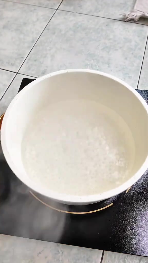 Periuk putih berisi air sedang menggelegak atas dapur elektrik dengan wap keluar