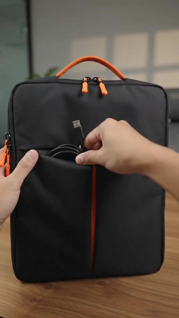 Poket depan beg laptop hitam dibuka dengan kabel USB disimpan di dalamnya, menunjukkan ruang organisasi aksesori