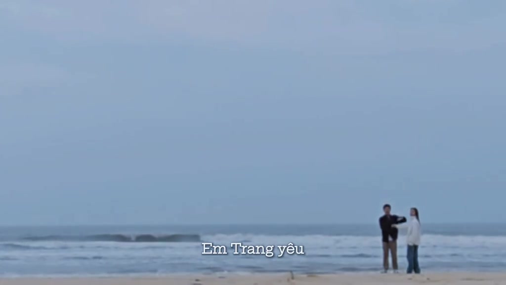 Khung hình viễn cảnh trong vlog cầu hôn được đăng lại trên TikTok: hai nhân vật đứng rất xa trên bãi biển, kèm phụ đề Em Trang yêu