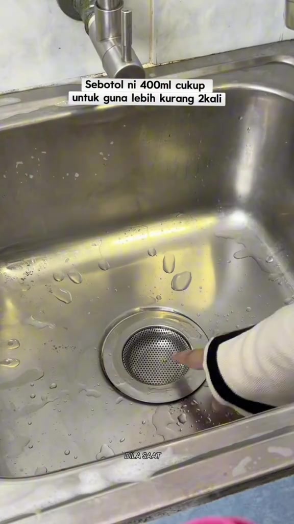 Sinki stainless bersih dengan bakul penapis berlubang halus dipasang pada lubang saliran, jari menunjuk ke arahnya