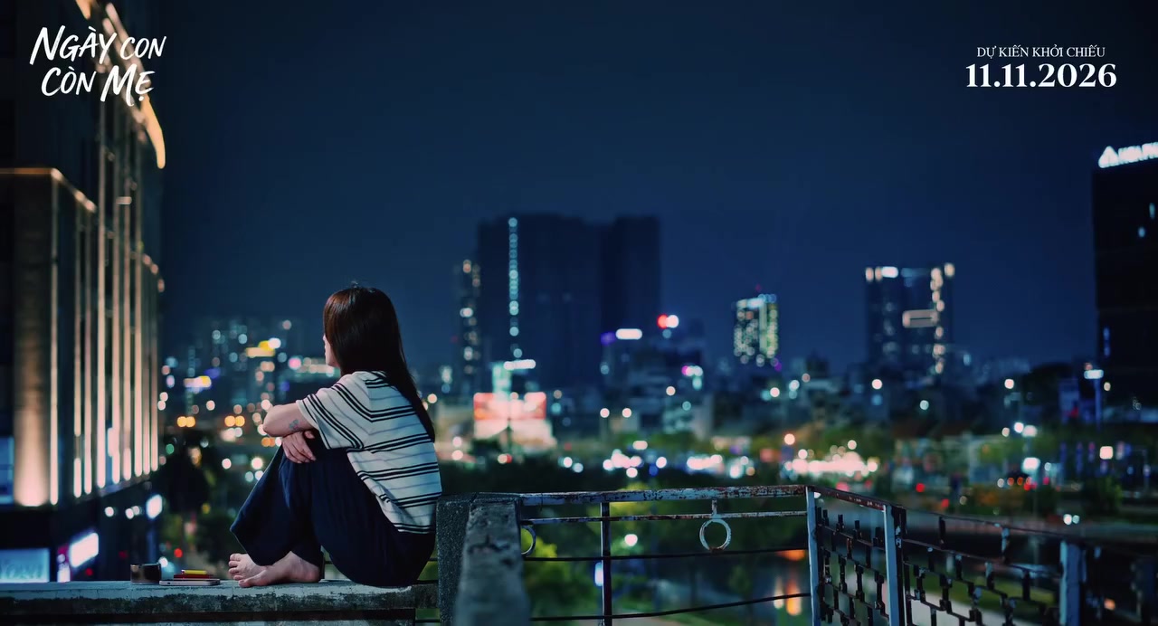 Nhân vật Mây ngồi co gối trên mép sân thượng nhìn ra phố đêm sáng đèn trong teaser trailer Ngày Con Còn Mẹ, chỉ thấy bóng lưng