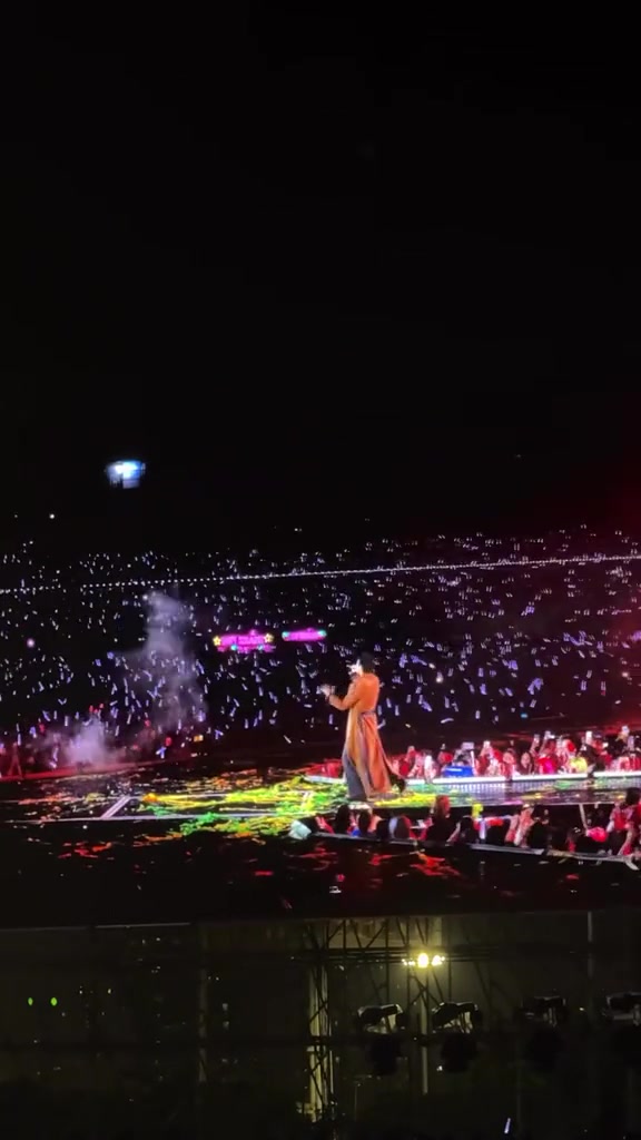Nghệ sĩ áo choàng dài đứng trên catwalk sân khấu concert Anh Trai Vượt Ngàn Chông Gai 2026, phía xa là hàng nghìn ánh lightstick trắng tím của khán đài