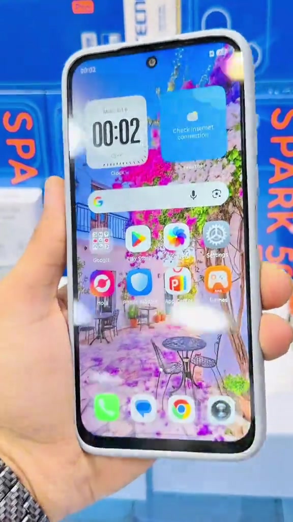 Bahagian depan telefon Tecno Spark 50 dengan skrin utama hidup dipegang di hadapan kotak biru Spark 50