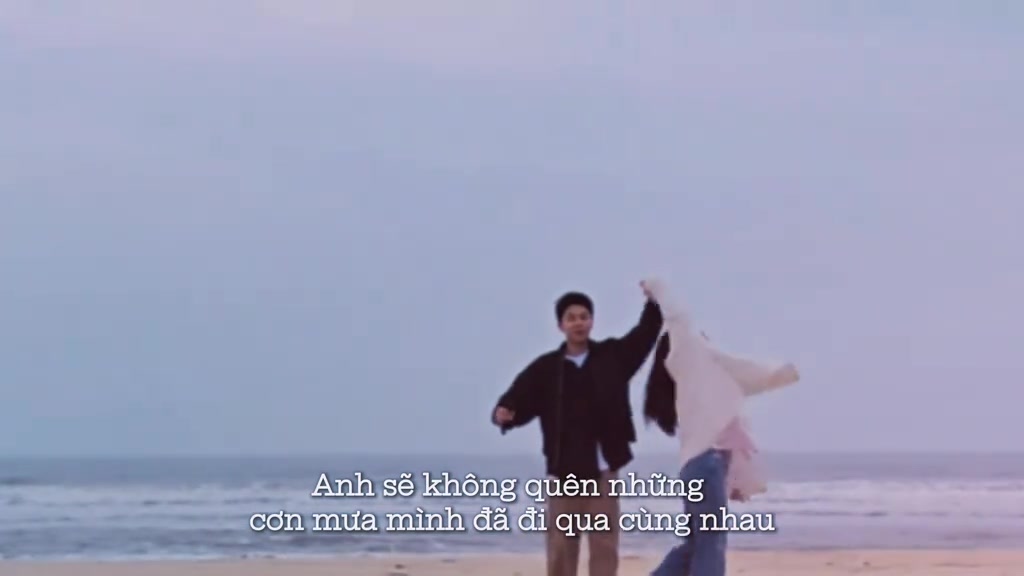 Khung hình trong vlog cầu hôn: hai nhân vật nắm tay xoay vòng trên bãi biển, kèm phụ đề Anh sẽ không quên những cơn mưa mình đã đi qua cùng nhau