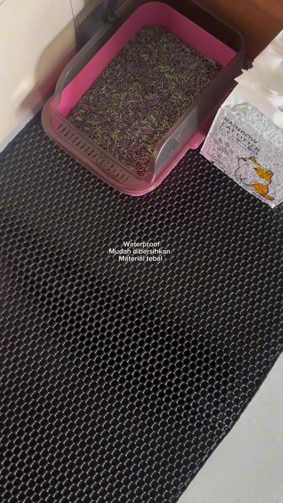 Kotak pasir merah jambu berisi pasir diletak atas tikar honeycomb hitam di penjuru rumah