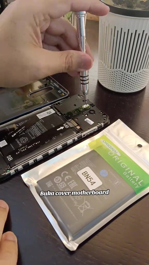 Pek bateri ganti berlabel ORIGINAL Battery BN54 di sebelah telefon yang sedang dibuka dengan pemutar skru