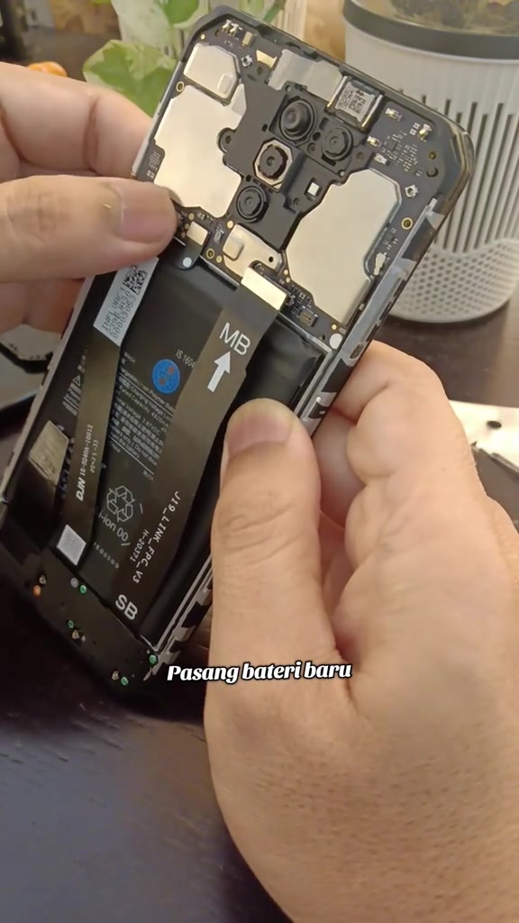Tangan memasang bateri baru ke dalam rangka telefon yang terbuka