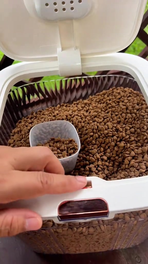 Bekas kedap udara terbuka penuh dengan kibbles dengan cup penyukat berisi kibbles di dalamnya